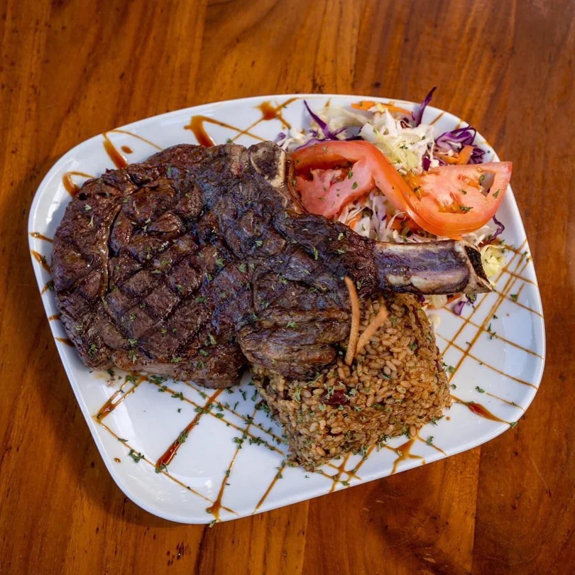 A large bone-in steak with a side of rice and fresh vegetables available at Terruno Restaurant.