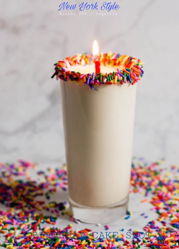 A birthday cake shot with a rim of sprinkles and a candle, made at New York Style sports bar.