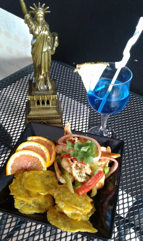 A seafood salad with a side of fried plantains and slices of orange and a blue mixed drink from New York Style sports bar..