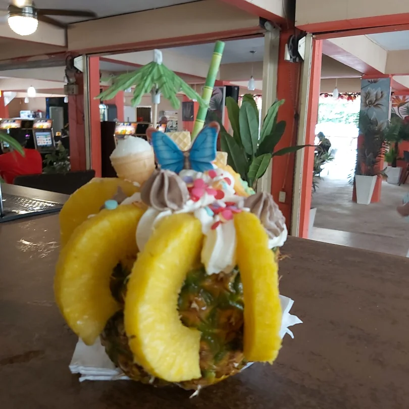 A tropical mixed drink served inside of a pineapple with whipped craem and sprinkles on top.