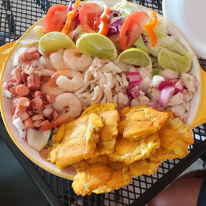 A large plate of food with fried plantains, fresh shrimp, a mixed salad, and lime wedges all in one big plate.