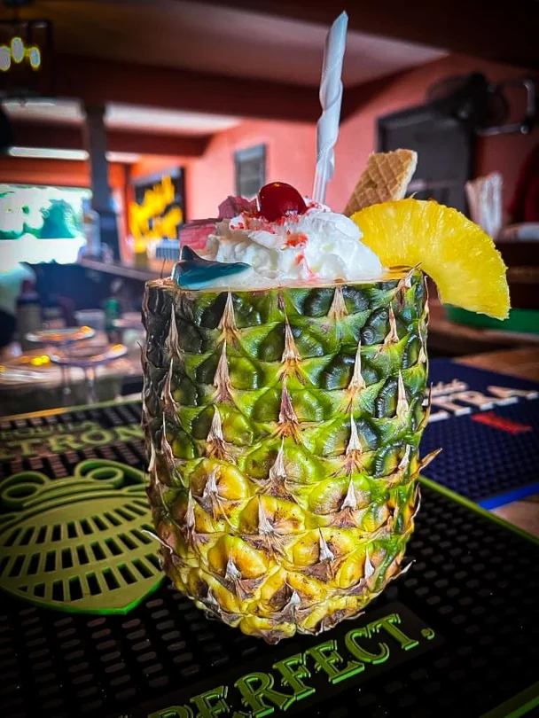 A mixed drink served inside of a hollow pineapple with whipped cream and fruit on top.